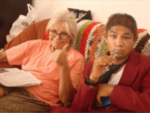 Two people sitting on a couch with one holding a cell phone.