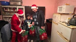 A man and woman in santa claus costumes handing presents to a child.