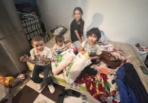 Children sitting on a mattress with bags.