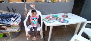 Child smiling with books at table outside.